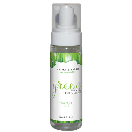 A clear plastic bottle with a white pump dispenser labeled 'Intimate Earth Green Foaming Toy Cleaner with Tea Tree Oil'. The label includes the product name and mentions it as a tea tree oil-infused cleaner.