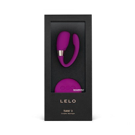 A deep rose-colored couples vibrator is displayed in its packaging. The box is black with gold accents, and the product has a sleek, modern design.