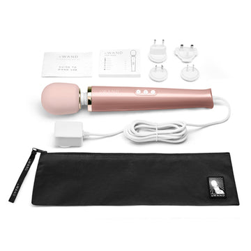 A rose gold Le Wand Plug-In Vibrating Massager with a sleek design, accompanied by a black carrying case, a USB charging cable, and an AC power adapter.