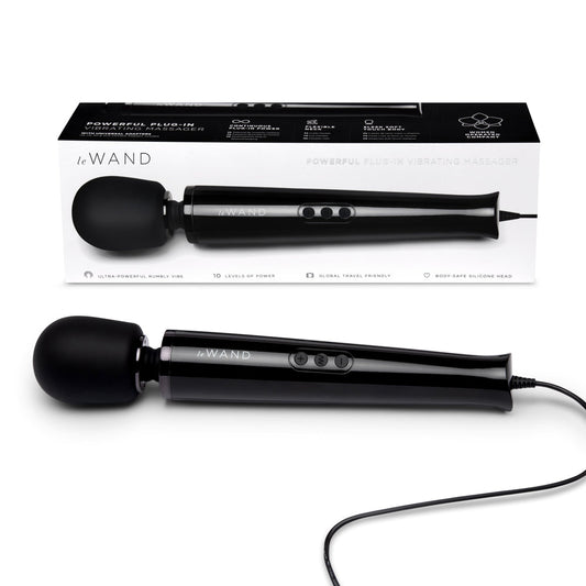 A black Le Wand Plug-In Vibrating Massager with a sleek design, showing the wand itself and the box in the background. The packaging highlights the product's features and includes a black silicone attachment.